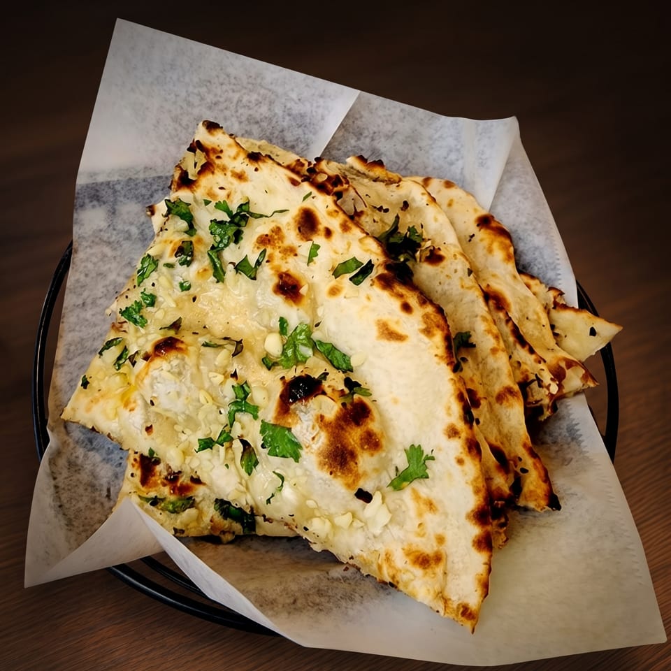 Several pieces of garlic naan with cilantro in a basket on a dark wooden table.
