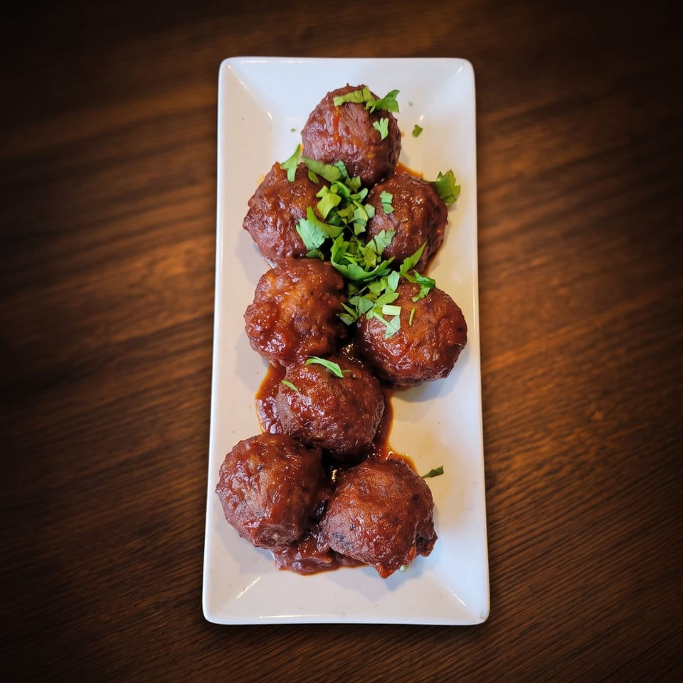 Meatballs in rich sauce garnished with fresh herbs on a white plate.